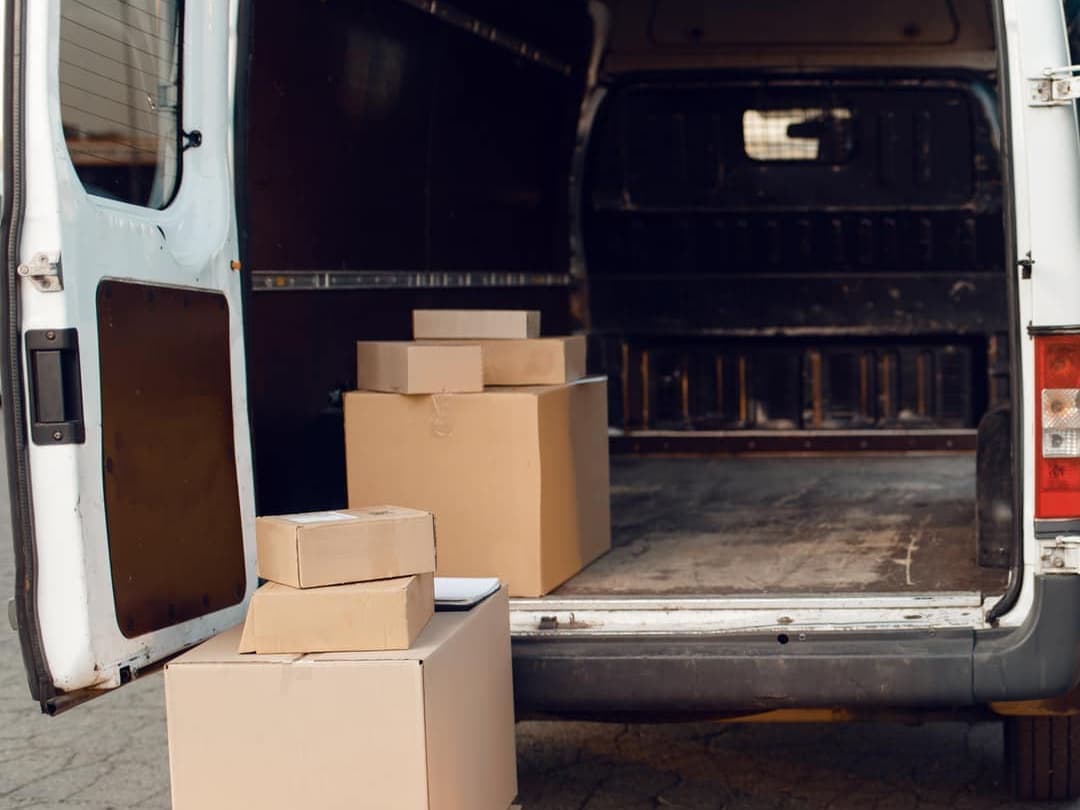 The open back of a white van, its empty load space behind a stack of cardboard boxes